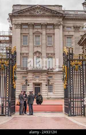 Looking through open front gates of Buckingham Palace, central London, UK. Armed police on guard checking security of visitors. Guarding royal family. Stock Photo