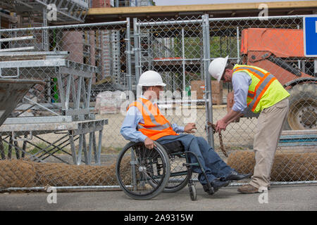 Two project engineers closing up at the job site, one in a wheelchair with a Spinal Cord Injury Stock Photo