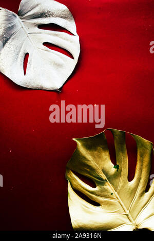 Exotic christmas celebration, two giant monstera leaves painted golden and silver with goldne christmas dcoration on a red background, top view, chris Stock Photo