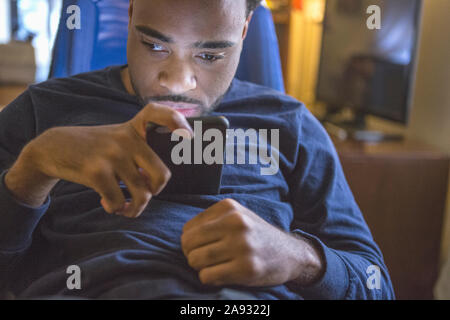 African American man with Cerebral Palsy using his cell phone at home Stock Photo