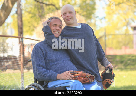 Happy father with Spinal Cord Injury and his son with Down Syndrome about to play baseball in park Stock Photo