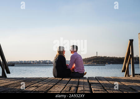 Couple sitting on jetty Stock Photo
