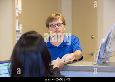 Young man with Down Syndrome giving out paperwork to his colleague in a health clinic Stock Photo