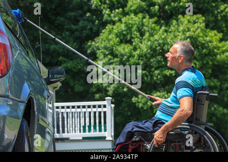 Man with a Spinal Cord Injury in wheelchair washing his accessible car Stock Photo