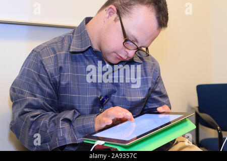 Hospital aid worker with Down Syndrome using a tablet in office Stock Photo
