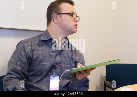 Hospital aid worker with Down Syndrome using a tablet in office Stock Photo
