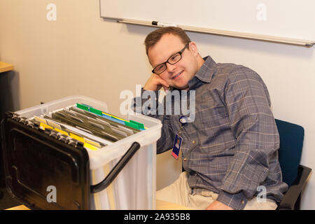 Hospital aid worker with Down Syndrome about to file paperwork in office Stock Photo