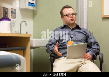 Hospital aid worker with Down Syndrome using a tablet in office Stock Photo