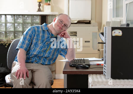 Man with Down Syndrome sitting at his computer in an office Stock Photo