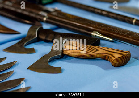 Two small axes with wooden handles on a table among knives and sabers. Close-up. Front view from above. Stock Photo