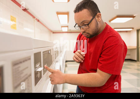 African American man with Down Syndrome paying for laundry in utility room Stock Photo