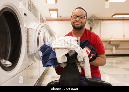 Happy African American man with Down Syndrome doing laundry in utility room Stock Photo