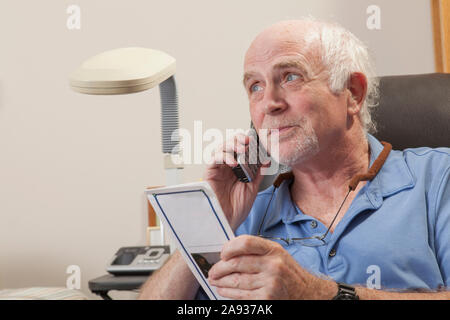 Man with Ataxia reading book and using his cell phone Stock Photo
