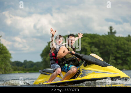 Young man with Down Syndrome riding on a jet ski with his friend in a lake Stock Photo