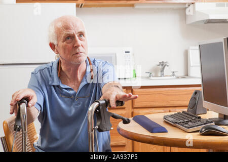 Man with Ataxia holding his walker with his computer in kitchen Stock Photo