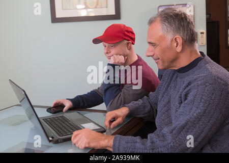 Young man with Down Syndrome and his father with Spinal Cord Injury using a laptop at home Stock Photo