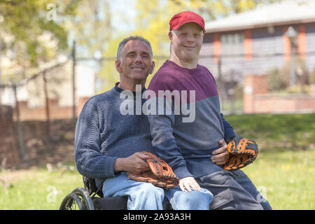 Happy father with Spinal Cord Injury and his son with Down Syndrome about to play baseball in park Stock Photo