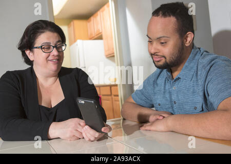 African American man with Down Syndrome using a cell phone with his mother at home Stock Photo