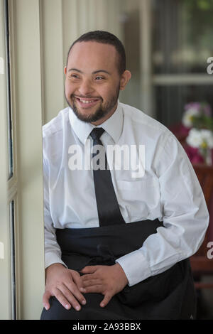 Happy African American man with Down Syndrome as a waiter in restaurant Stock Photo