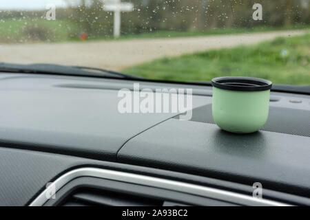 View looking through the car windscreen on a rainy day, with a green flask drinking cup on the dashboard. Stock Photo