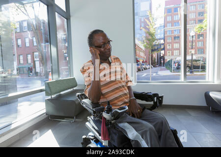 Man with Guillain-Barre Syndrome on wheelchair in front of the apartment window Stock Photo