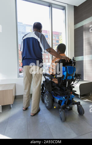 Man with Guillain-Barre Syndrome with his father looking out through the apartment window Stock Photo