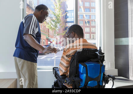 Man with Guillain-Barre Syndrome with his father looking out through the apartment window Stock Photo