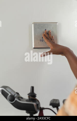 Man with Guillain-Barre Syndrome in his power chair pressing button for elevator Stock Photo