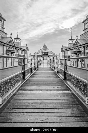 Eastbourne pier with a walkway to a cafe.  Shops with pagoda style domes are on wither side and a cloudy sky is above. Stock Photo