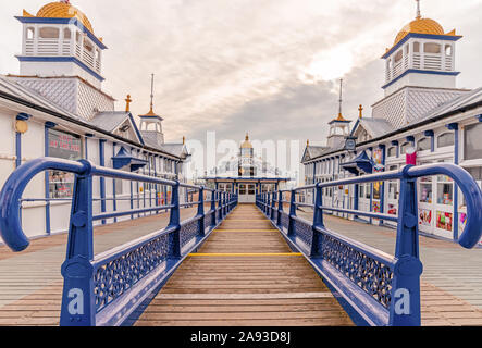 Eastbourne pier with a walkway to a cafe.  Shops with pagoda style domes are on wither side and a cloudy sky is above. Stock Photo