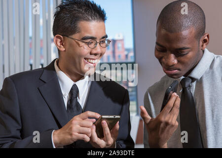 Two men with Autism looking at their texts on mobile phones in an office Stock Photo