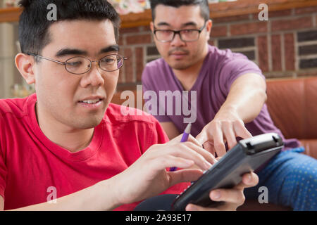 Asian man with Autism working on his homework with his brother on a phone Stock Photo