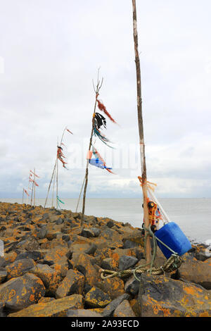 Poles with colored rope and plastic waving in the wind on breakwater or pier with yellow lichen at the entrance to the port of Harlingen Stock Photo
