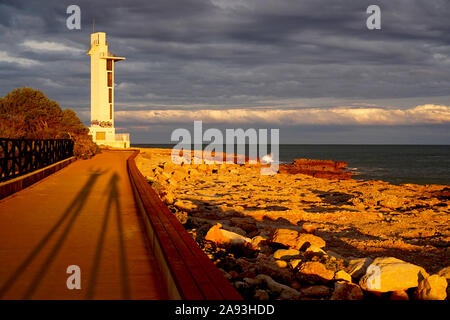Shadow figures of a couple at sunset by a coastal scene with lighthouse Stock Photo