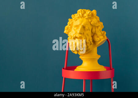 Yellow male head with beard and long hair of the ancient sculpture on a red stand against blue wall Stock Photo