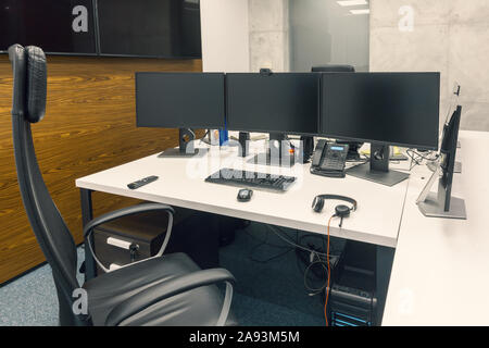 dvelopers desktop with three black monitors in office. empty chair Stock Photo