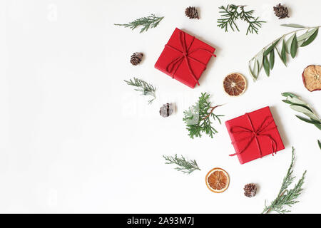 Christmas festive composition, pattern. Olive, cypress tree branches, pine cones, red gift boxes, dry apple, orange fruit on white background. Winter Stock Photo