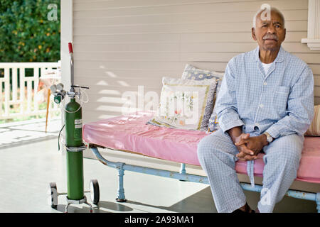 Elderly man sitting on the deck of rest-home next to oxygen bottle. Stock Photo