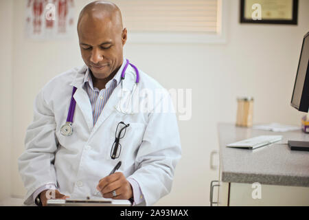 Male doctor taking notes on a clipboard inside his office. Stock Photo