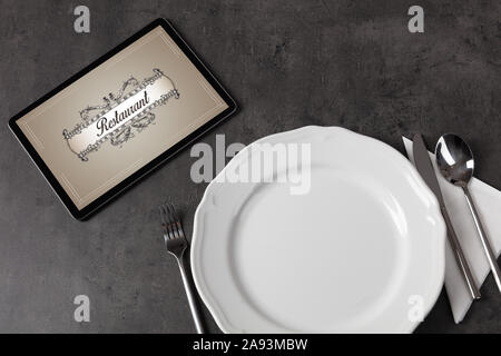 Tablet with stylish restaurant logo and laid table Stock Photo