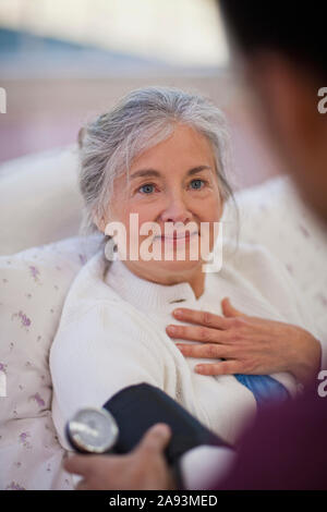 Hopeful senior woman looking at a male nurse while having her blood pressure taken Stock Photo