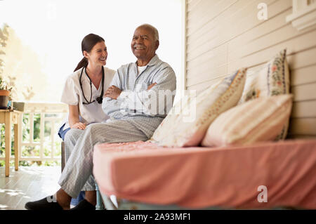 Smiling elderly man sitting on the deck of rest-home with his nurse Stock Photo