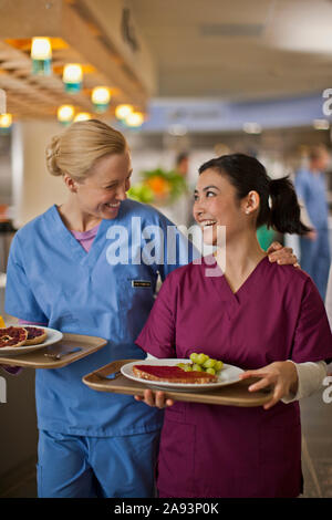 Two young nurses smile and chat together as they get their lunch from the hospital canteen Stock Photo