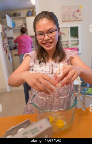 Teenage girl who has Learning Disability cracking eggs for cooking Stock Photo