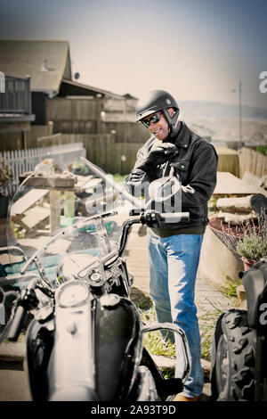 Smiling man wearing a helmet and gloves while standing next to a motorcycle outside his home. Stock Photo