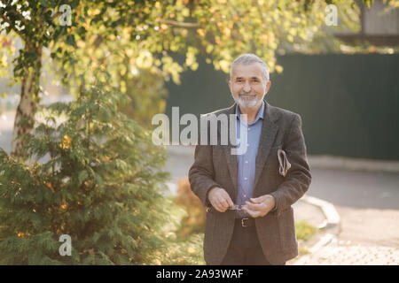 Handsome senior man walk through the park with newspaper in hands. Bearded grandpa early in the morning walking in the park Stock Photo