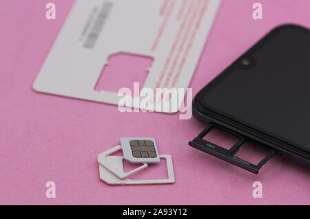 Smart phone next to a sim card to connect to the mobile phone network, on a pink surface Stock Photo