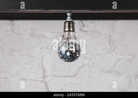 Light bulb with nuts and bolts against white brick wall. Handmade unusual object. Collecting ideas concept photo. Creative person concept. Stock Photo
