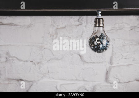 Light bulb with nuts and bolts against white brick wall. Handmade unusual object. Collecting ideas concept photo. Creative person concept. Copy space. Stock Photo