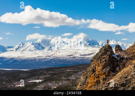 A hiker stands atop a rock outcropping on Donnelly Dome while taking in the view of Mount Moffit and the Alaska Range Stock Photo